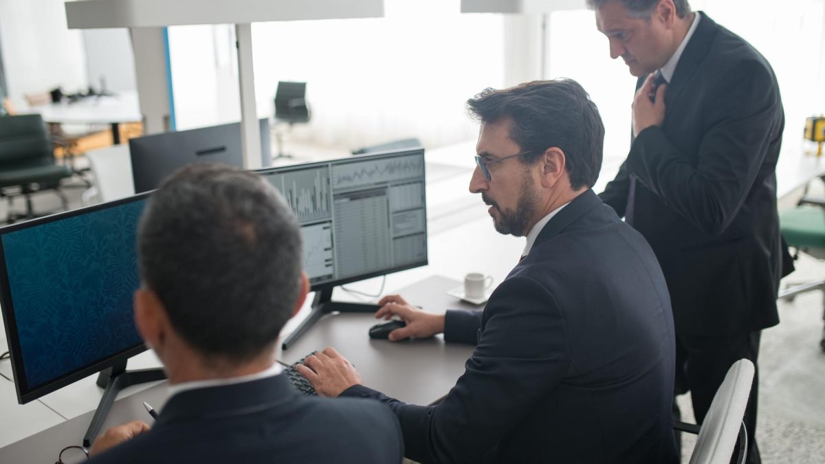 Business professionals analyzing data on computer monitors, reflecting the role of ai security in investment decisions.