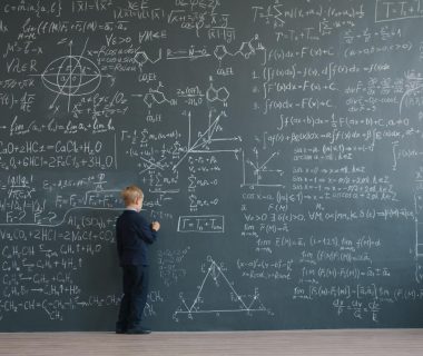 A young child in a suit demonstrates problem-solving on a chalkboard, symbolizing human intuition in math as AI agents advance.