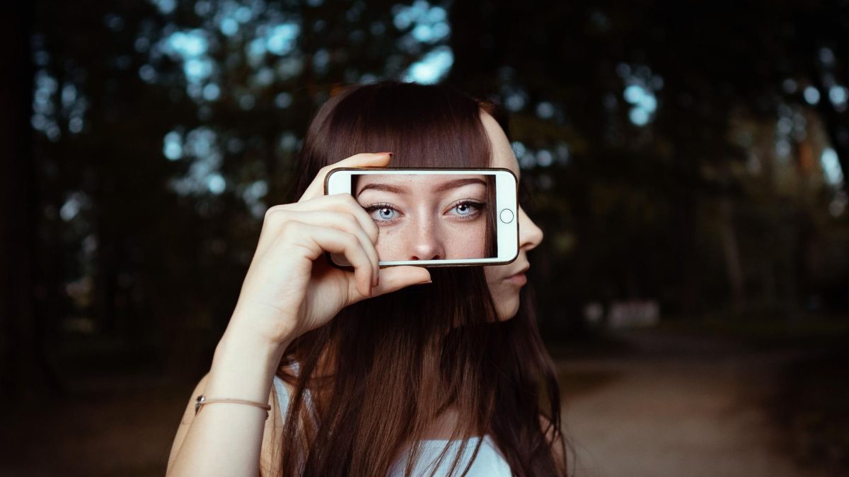 Young woman using iPhone 18 Pro to verify image authenticity amid deepfake concerns.