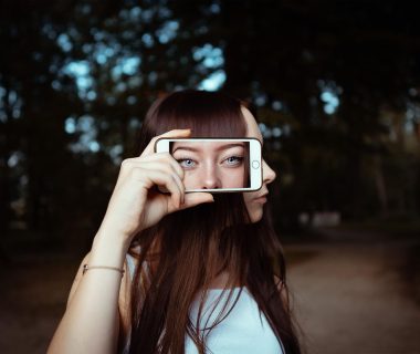 Young woman using iPhone 18 Pro to verify image authenticity amid deepfake concerns.